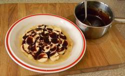 pancakes on a white plate covered with slices of banana and hot chocolate sauce