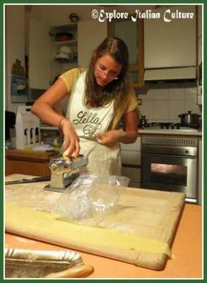 A woman in a kitchen putting pasta dough into the pasta machine