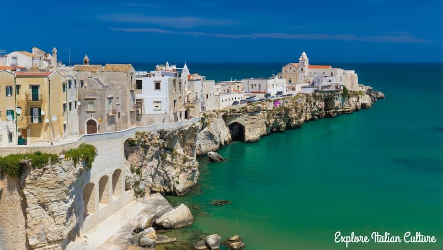 Old village perched on cliff overlooking blue sea.